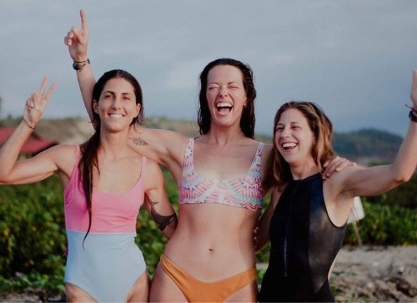 3 friends laughing by the beach on a women's surf trip